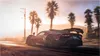 A red sports car driving on a road with palm trees and a sunset in the background. Produktbild-Vorschau