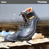 A pair of black work boots with orange accents are shown resting on a textured surface, possibly part of a vehicle or machinery. Produktbild-Vorschau