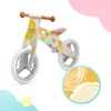 A wooden balance bike with a yellow and white pattern, shown against a white background with soft pastel shapes. Náhľad obrázku produktu