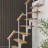 A spiral staircase with wooden steps and white metal supports against a dark wood paneled wall and a white wall, with some greenery on the right. Produktbild-Vorschau