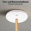 A smoke detector is shown mounted on a ceiling, with a wooden pole extending from its center, suggesting a test or mute function. Produktbild-Vorschau