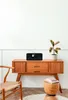 A black DAB+ radio sits on a wooden cabinet next to a plant. Produktbild-Vorschau