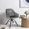 A gray velvet swivel chair with black metal legs is shown in a room setting, next to a small wooden side table with a vase of flowers and a decorative bowl. Produktbild-Vorschau