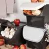 A kitchen scene with stacked storage containers for vegetables and fruits, with apples and garlic visible. Anteprima dell’immagine prodotto
