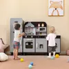 Two children playing with a wooden toy kitchen set, which includes a refrigerator, stove, microwave, and washing machine. Náhled obrázku produktu