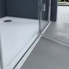 A close-up view of a modern shower enclosure, showing the corner where the glass meets the shower tray and the floor. Produktbild-Vorschau