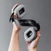 Hands holding a black gaming headset with gray earcups. Produktbild-Vorschau