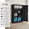 A black metal filing cabinet with its door open, filled with folders, trays, and boxes. A text overlay on the left describes the features of the cabinet. Produktbild-Vorschau