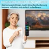 An elderly woman is holding a remote control and pointing at it, with a television in the background. Produktbild-Vorschau