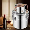 A stainless steel distiller sits on a wooden surface next to a bottle of red wine and a glass of wine, with a wooden barrel in the background. Náhľad obrázku produktu