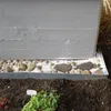 A close-up view of a metal garden border separating soil from a decorative stone and gravel bed against a concrete wall. Produktbild-Vorschau