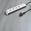A white and black power strip with four outlets and a detached plug lies on a gray wooden surface. Náhľad obrázku produktu