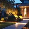 A modern house exterior at dusk with landscape lighting illuminating the garden and pathway. Produktbild-Vorschau