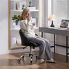 A woman sitting in a chair by a desk, drinking from a mug. Produktbild-Vorschau