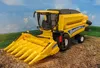 A toy model of a New Holland combine harvester for corn, displayed on a dirt surface with a backdrop of fields and sky. Voir les images du produit