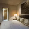 A bedroom scene with a bed, nightstand, lamp, and artwork. Anteprima dell’immagine prodotto