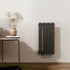 A vertical panel radiator mounted on a light gray wall, next to a small side table with books and a vase of dried flowers. Produktbild-Vorschau