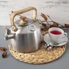 A kettle, cup of tea, and cookie are arranged on a woven placemat. Voir les images du produit