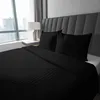 A black satin duvet cover and pillowcases are neatly arranged on a bed with a grey upholstered headboard, next to a window with a city view. Produktbild-Vorschau
