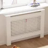 A white radiator cover with a slatted front is placed in front of a window, with a book and decorative object on the windowsill above. Náhľad obrázku produktu