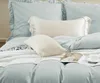 A neatly made bed with light blue bedding, pillows, and a white knitted blanket. Produktbild-Vorschau