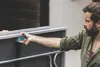 A man is holding a blue object against the side of a gray table tennis table. Produktbild-Vorschau