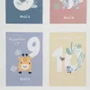 A collage of four baby milestone cards, each featuring a cartoon animal and a number. Anteprima dell’immagine prodotto