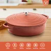 A red Dutch oven is displayed on a wooden table in a kitchen setting. The bottom of the image features icons indicating compatibility with various heat sources. Produktbild-Vorschau