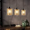 A dining table with three pendant lights hanging above it, and decorative bottles on the table. Produktbild-Vorschau