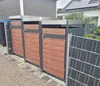 Three modern trash bin enclosures with wood-look doors are lined up next to a building and a fence. Produktbild-Vorschau