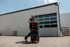 A man is pushing a stack of toolboxes on wheels in front of a warehouse. Produktbild-Vorschau