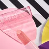 A close-up shot of a pink lipstick and a clear lip gloss with glitter, arranged on a pink circular surface with a black and white striped background. Produktbild-Vorschau