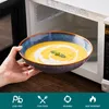 A hand is holding a bowl of soup in front of an open microwave. Náhled obrázku produktu