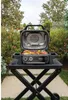 An outdoor scene with a grill on a stand, surrounded by greenery and flowers. Náhľad obrázku produktu