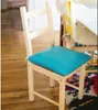 A close-up of a wooden chair with a turquoise cushion, placed on a wooden floor next to a colorful rug. Produktbild-Vorschau