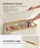 A person's hands are shown opening the lid of a cream-colored laundry basket with a bamboo trim. The basket contains folded towels. A close-up of the basket's faux leather logo is also shown. Produktbild-Vorschau