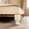 A close-up view of a carved wooden furniture leg attached to a bed frame, set in a room with ornate decor. Podgląd zdjęcia produktu