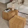 Two square wooden coffee tables are placed on a light gray floor in front of a white sofa. A vase with branches and berries sits on one of the tables. Produktbild-Vorschau