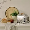 A kitchen counter scene with a Dualit toaster, bread, jam, and a plant. Anteprima dell’immagine prodotto