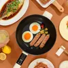 Schwarze elektrische Pfanne mit weißem Griff, kocht zwei Spiegeleier und drei Würstchen, umgeben von anderen Gerichten Produktbild-Vorschau