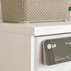 Close-up of the top of a white washing machine with a beige laundry basket on top and the control panel visible. Podgląd zdjęcia produktu