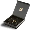A black gift box is open, revealing a black leather necklace with a gold cross pendant inside. Produktbild-Vorschau