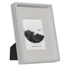 A white picture frame with a black stand, displaying a black and white photograph of a forest. Produktbild-Vorschau