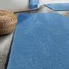 A blue bath mat is shown in a bathroom setting next to a bathtub and a woven stool. Anteprima dell’immagine prodotto
