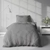A neatly made bed with gray bedding in a room with a brick wall and natural light casting shadows. Produktbild-Vorschau
