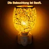 A mosaic-patterned electric aroma diffuser lamp plugged into a wall socket, emitting a warm yellow glow. Produktbild-Vorschau