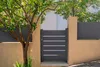 A modern gray garden gate with horizontal silver accents, set within a beige stucco wall and flanked by a tree and a section of gray fencing. Produktbild-Vorschau