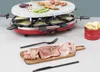 A red raclette grill with a stone top, set up for cooking, with food items and utensils laid out on a wooden board in the foreground. Produktbild-Vorschau