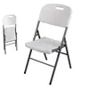 A white folding chair is shown from a slightly angled front view, with a smaller, folded version of the same chair visible in the background to the left. Produktbild-Vorschau