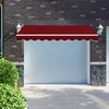 A red awning is installed above a white garage door, with a brick wall and some greenery visible. Produktbild-Vorschau
